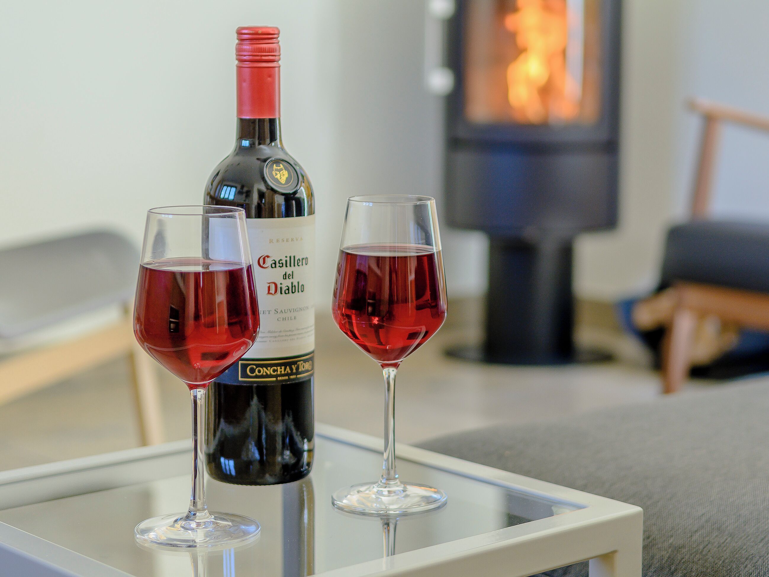 En flaske Casillero del Diablo vin og to glas på et glastop i en stue med pejs.