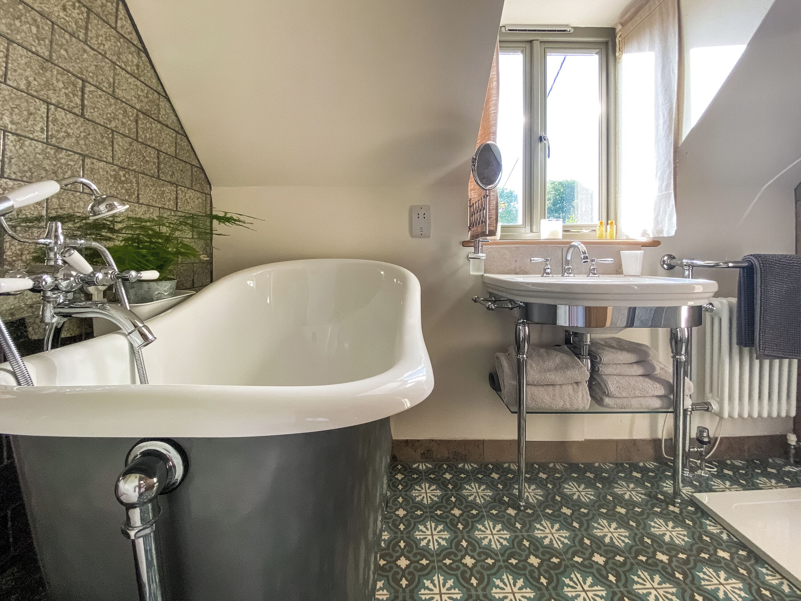 Une salle de bain avec une baignoire sur pieds, un lavabo et une fenêtre laissant entrer la lumière naturelle.