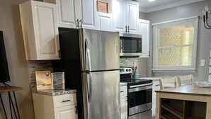 A modern kitchen with white cabinets, stainless steel appliances, a wooden floor, and a dining area with a bench. - Apple Valley 23 at Rumbling Bald (Lake Lure)