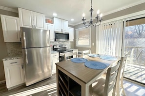 A kitchen with white cabinets, stainless steel appliances, a dining table with blue placemats, and a chandelier.