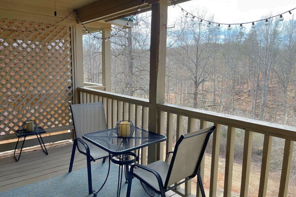 A covered outdoor seating area with a table and chairs, a lattice screen, and a view of trees.