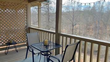 A covered outdoor seating area with a table and chairs, a lattice screen, and a view of trees.