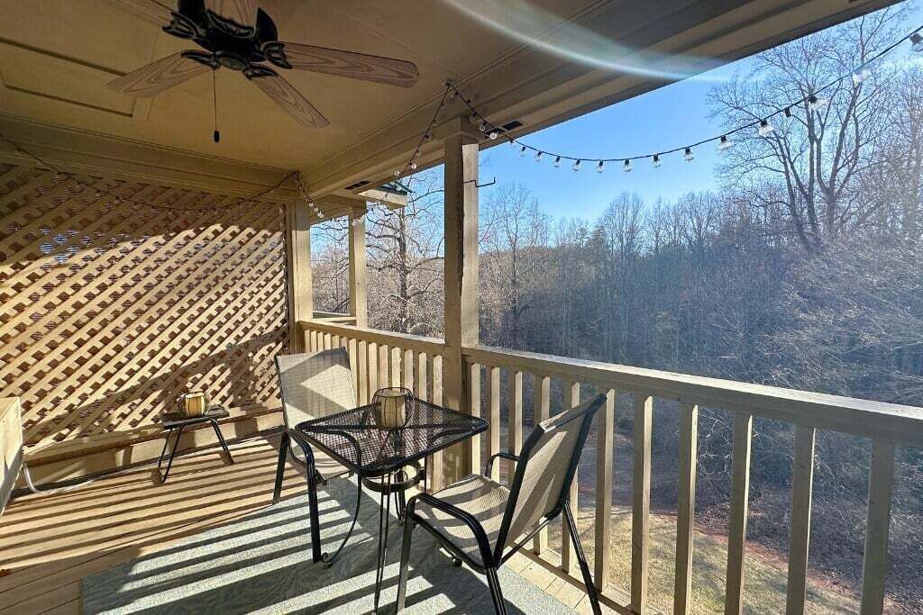 A covered outdoor area with a table and chairs, a ceiling fan, and a view of trees.