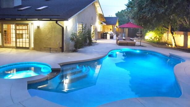 A swimming pool with a curved design, surrounded by a patio area with outdoor furniture. - A Luxury Home with Pool, Spa, and Mini-golf (Los Angeles)