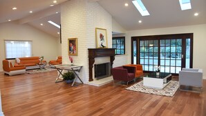 A spacious living room with a fireplace, modern furniture, and large windows offering a view of the outdoors. - A Luxury Home with Pool, Spa, and Mini-golf (Los Angeles)