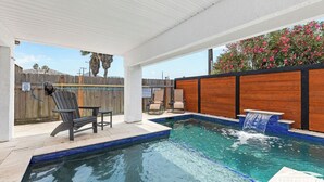 A swimming pool with a wooden deck, lounge chairs, and a waterfall feature. - Remodeled Townhome • Covered Heated Pool • 2 Minute Walk to Beach (South Padre Island)