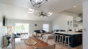 A modern kitchen with a dining area, featuring a wooden table, bar stools, and a ceiling fan. - Remodeled Townhome • Covered Heated Pool • 2 Minute Walk to Beach (South Padre Island)