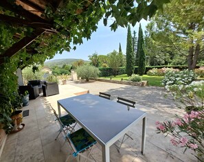Eine Terrass mit Tisch und Stühlen, umgeben von Grünpflanzen und Blick auf die Landschaft.