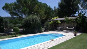 Una piscina con piastrelle in pietra, circondata da un prato curato e diversi alberi.