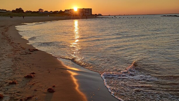 Uma praia ao pôr do sol, com um edifício ao fundo.