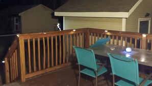 Um deck de madeira com mesa, cadeiras, corrimão e uma casa ao fundo.