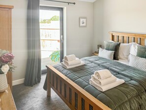 Une chambre à coucher comprenant un lit, une table de chevet, une commode, une fenêtre avec des rideaux et une vue sur l’extérieur.