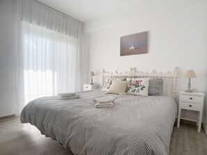 A bedroom with a large bed, two bedside tables, a nightstand, a window with sheer curtains, and a painting on the wall. - AP241 - Verdemar (Nerja)
