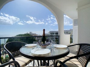 A round table with four white plates, a bottle of champagne, and a decorative bowl on a balcony overlooking a cityscape. - AP241 - Verdemar (Nerja)