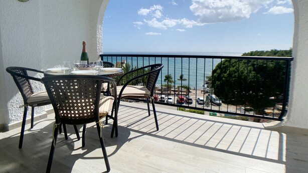 Ein Balkon mit Tisch für zwei Personen, mit Blick auf einen Strand und das Meer.