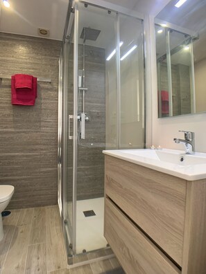 A modern bathroom with a glass shower enclosure, a white sink, and a wooden vanity. - AP241 - Verdemar (Nerja)