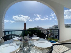 A table set for two with a bottle of champagne, a bowl, and plates, overlooking a pool and buildings. - AP241 - Verdemar (Nerja)