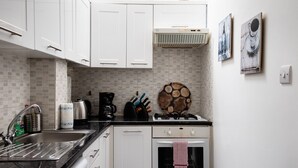 A modern kitchen with white cabinets, a black countertop, a coffee maker, a kettle, and a stove.