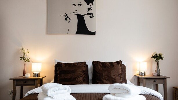 A neatly made bed with brown and white bedding, two bedside tables with lamps, and a wall-mounted artwork.