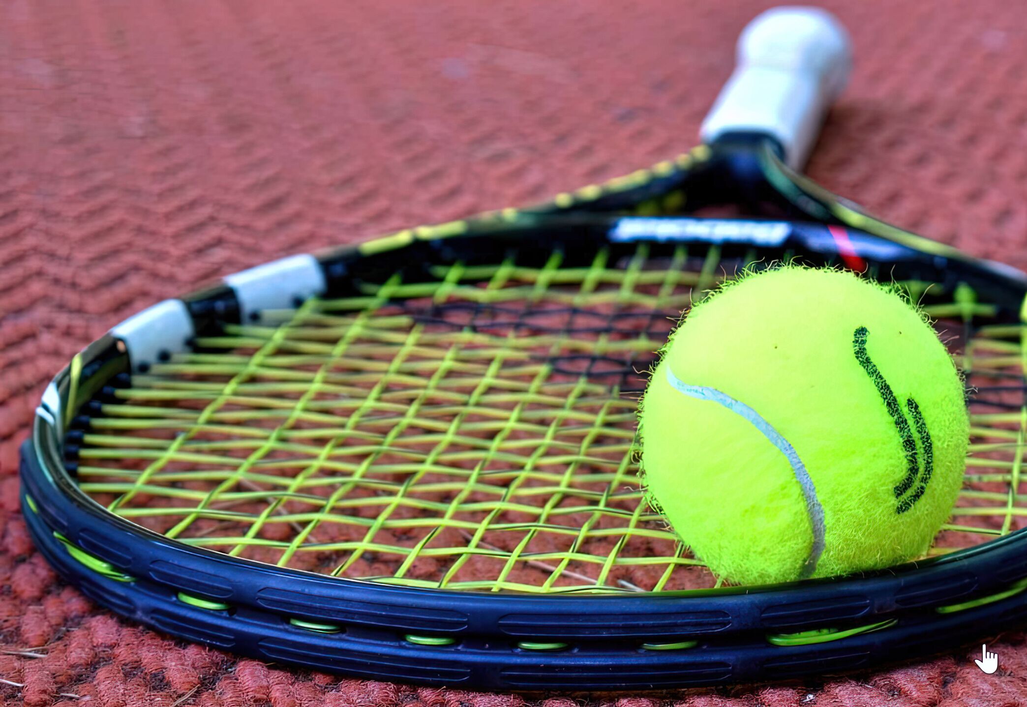 A tennis racket and ball on a red textured surface.