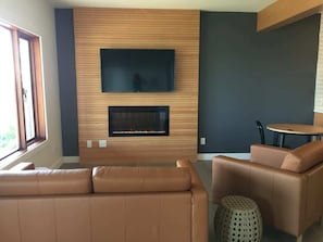 Uma sala de estar moderna com uma televisão de tela plana acima de uma lareira, sofás de couro e uma mesa de centro redonda.