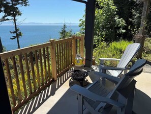 A deck with a view of the sea, a grill, and two Adirondack chairs.