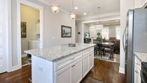 Una cocina con armarios blancos, encimeras de granito, un refrigerador de acero inoxidable e iluminación colgante.