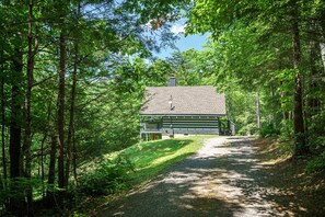 A cabin with a gravel path leading to it, surrounded by dense forest.