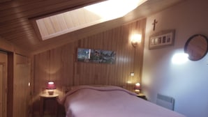 Ein Schlafzimmer mit Holzboden, einem Bett mit rosa Decke, zwei Nachttischlampen, einer Wanduhr und einem gerahmten Bild.