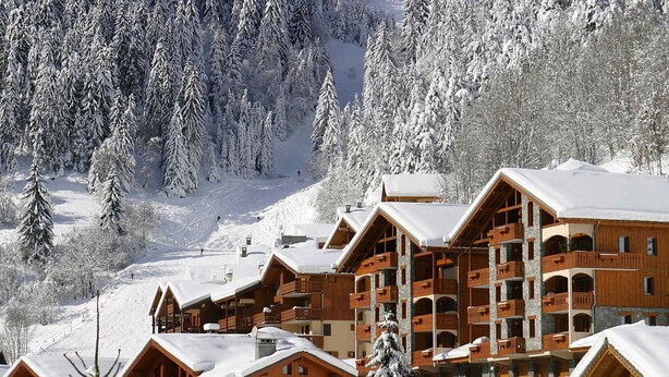 Ein schneebedecktes Chalet mit mehreren Holzhäusern, jedes mit Balkonen und einer Steinfassade.