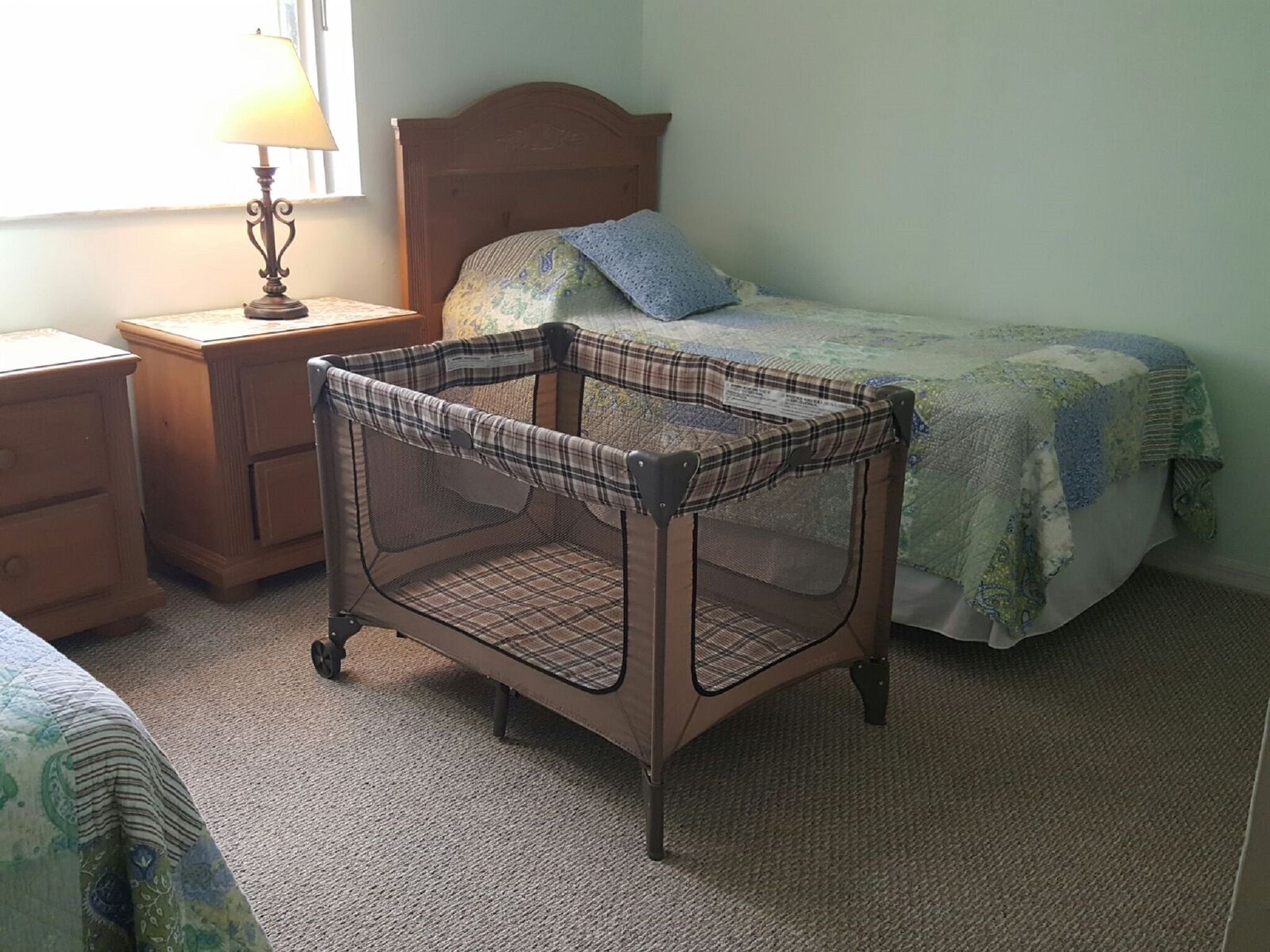 Un dormitorio con una cama de madera, una mesita de noche con una lámpara y una cuna para bebé.