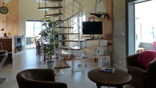 A spacious living area with a spiral staircase, a television, and a dining table.