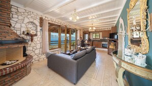 A spacious living area with a stone fireplace, a sofa, and a view through large windows.