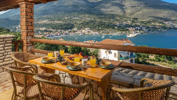 A wooden table with chairs and a view of a coastal town and mountains.