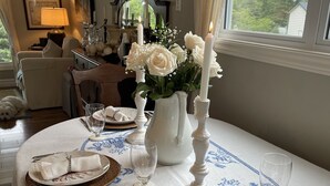 Una mesa de comedor dispuesta con platos blancos, cubiertos y un florero con flores y velas blancas.