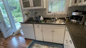 Una cocina con gabinetes blancos, encimera de granito, lavavajillas integrado y cafetera.