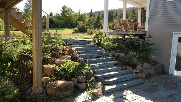 Un sendero de piedra que conduce a una terraza de madera con mobiliario exterior.