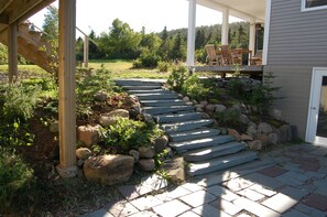 Ein gepflasterter Weg führt zu einer Holzterrasse mit Gartenmöbeln.