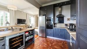 Een moderne keuken met een ingebouwde oven, een grote koelkast en een eethoek met een televisie en natuurlijk licht.