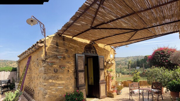 Un edificio rústico de piedra con techo de paja, patio, mobiliario exterior y plantas en macetas.