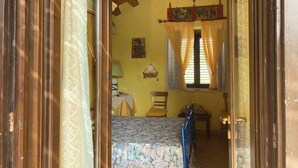 Una habitación con una cama, techo de madera, ventana con cortinas y una lámpara en la pared.
