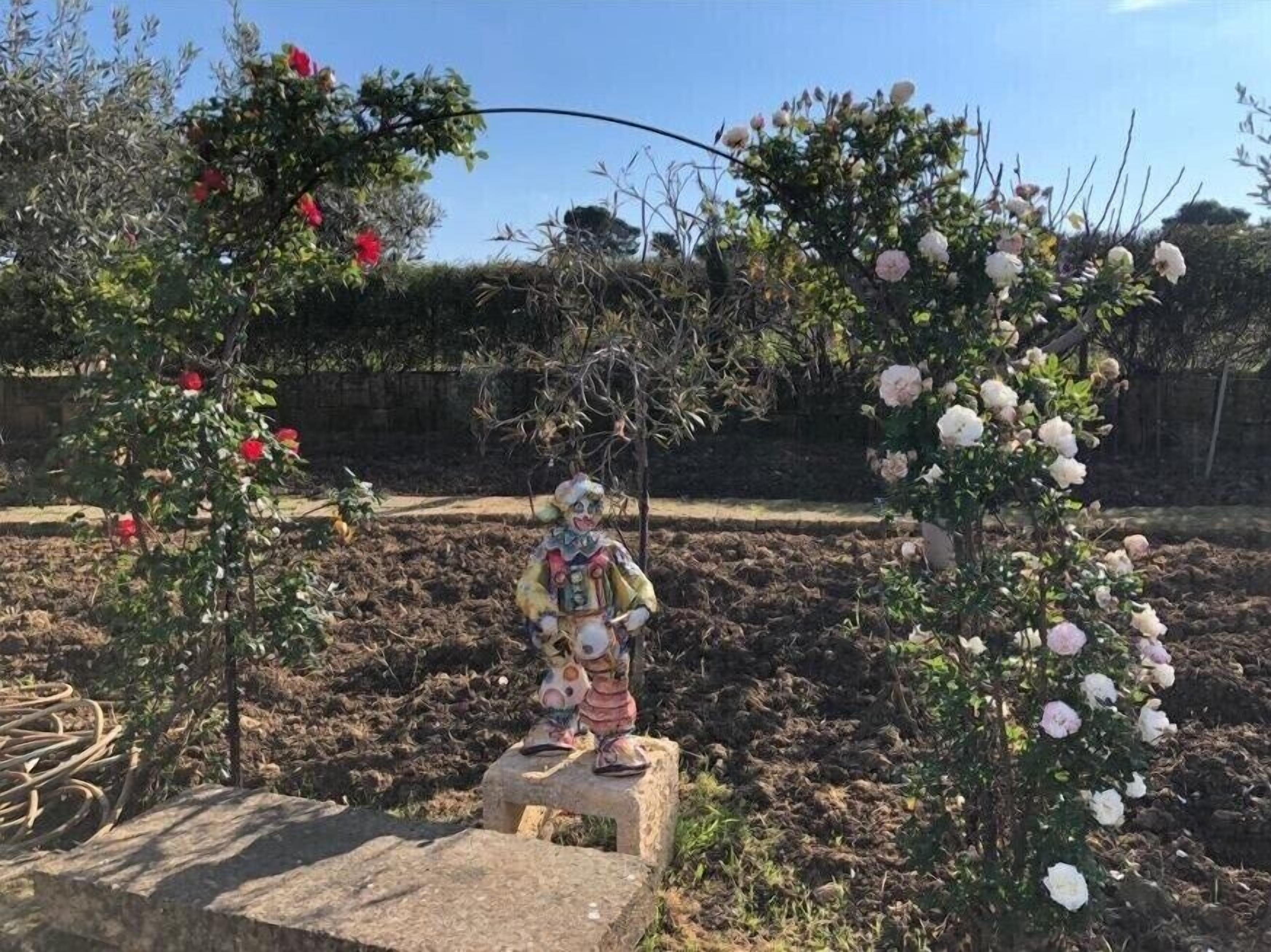 A garden with a statue of a clown on a stone pedestal surrounded by flowering bushes.
