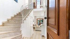 Una scala conduce al secondo piano, con una porta in legno e vista su un soggiorno con divano e tavolino.