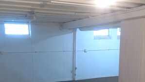 Une pièce avec une moquette sombre, des murs blancs, une porte et une fenêtre.
