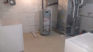Une pièce utilitaire équipée d’un chauffe-eau, d’un réfrigérateur blanc et d’une pompe à eau.
