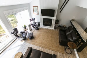 Uma sala de estar moderna com lareira, sofás de couro, uma TV grande e vista para o exterior.