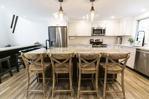 Uma cozinha moderna com armários brancos, eletrodomésticos de aço inoxidável e uma mesa de jantar de madeira com quatro cadeiras.