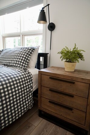 Quarto com cama, mesa de cabeceira, abajur e planta em vaso.