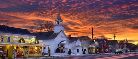 A town with a church and buildings along a snow-covered street during sunset.