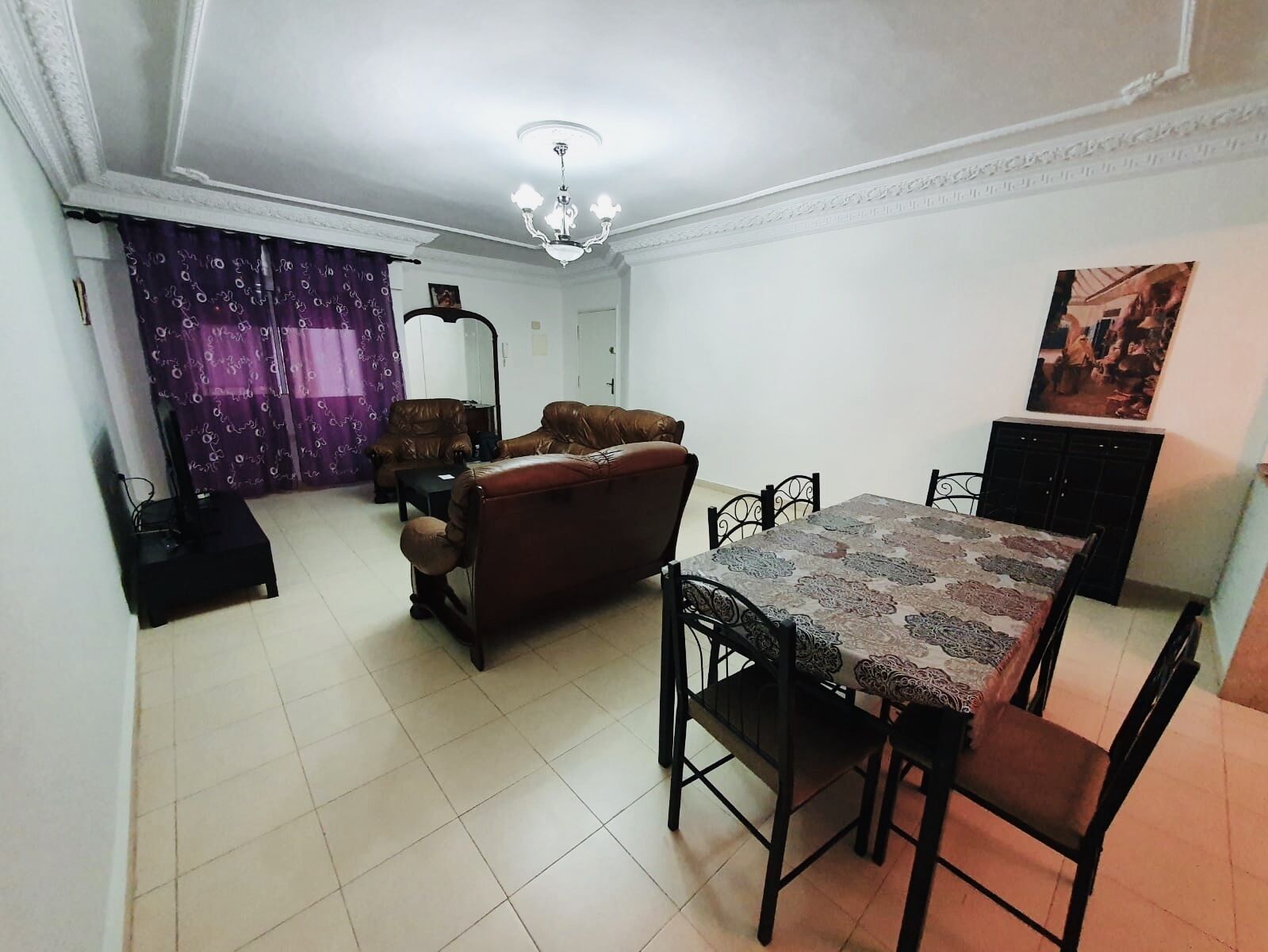 A dining area with a table and chairs, a sofa, and a lamp.